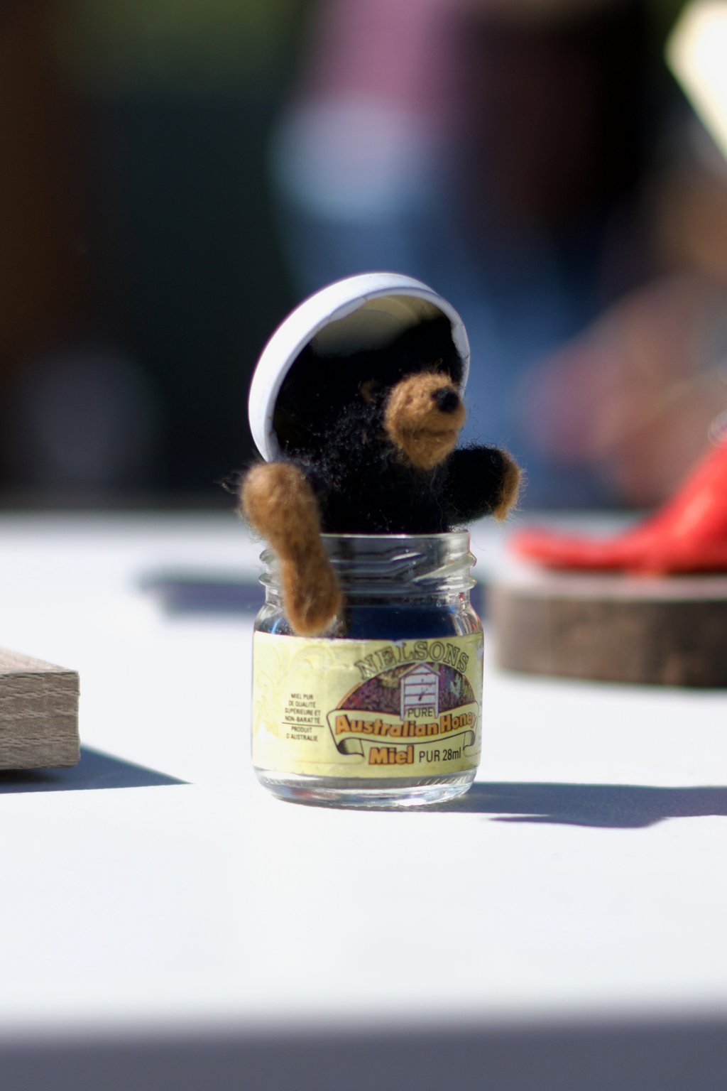 A photo of a felt bear with its arms spread sitting in a small glass honey jar