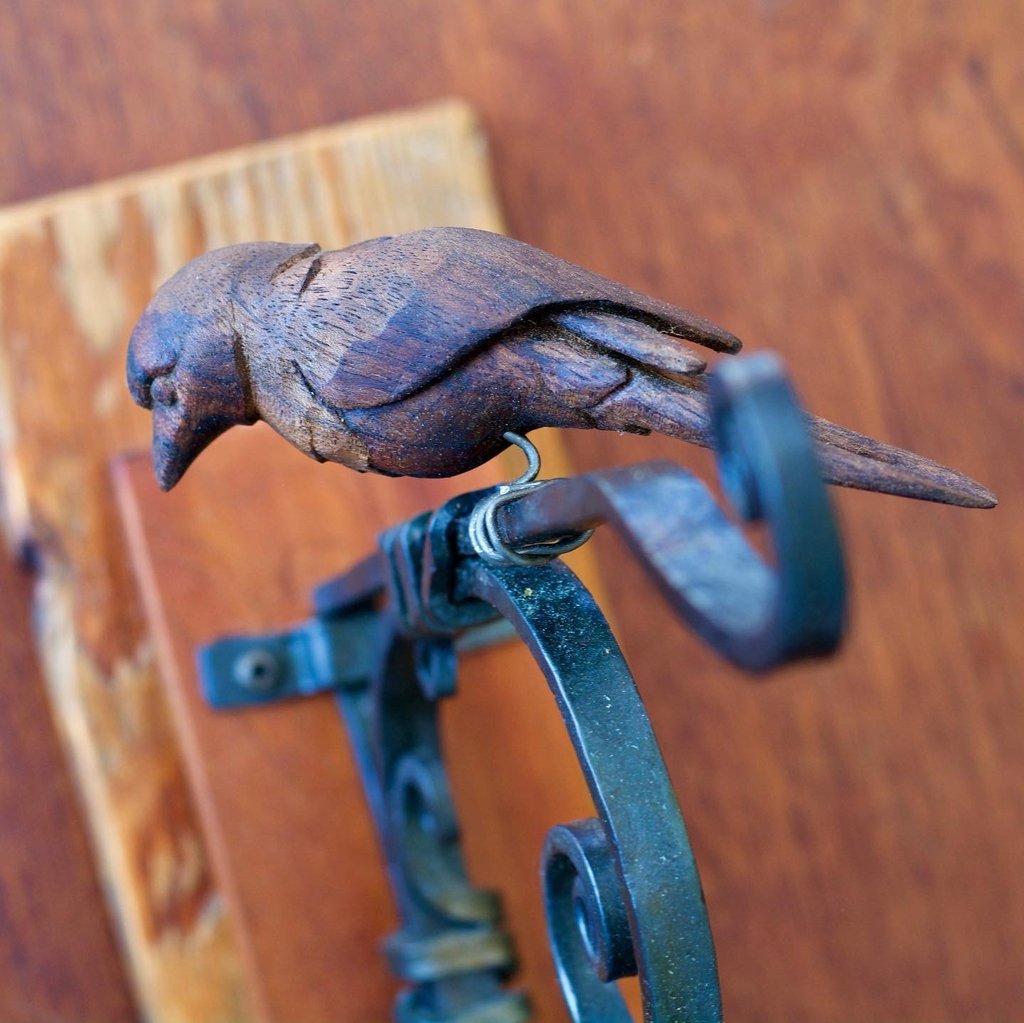 A photo of a small carved bird perched on a metal hook