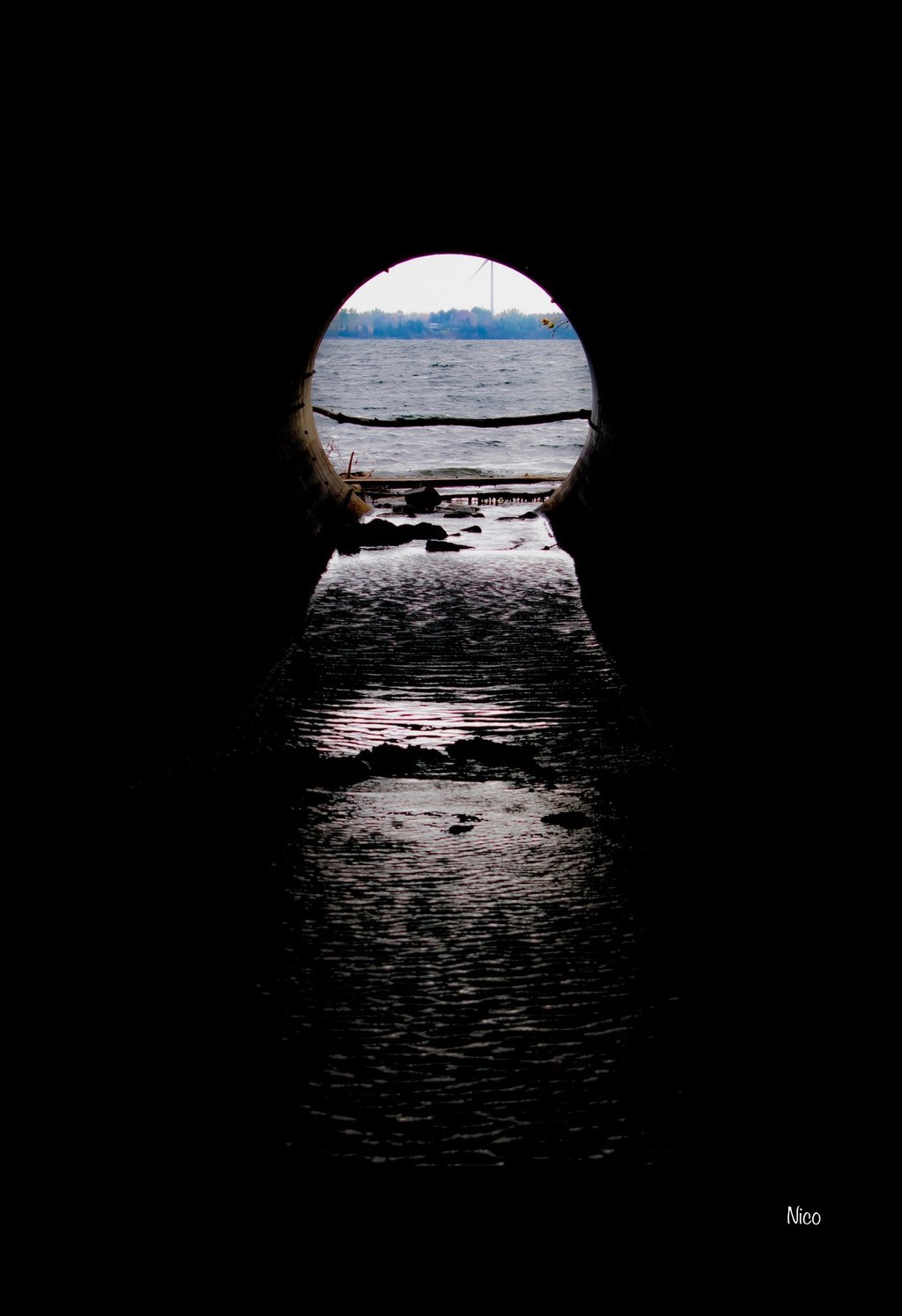 A photo from the inside of a tunnel, looking out through the opening at a choppy lake